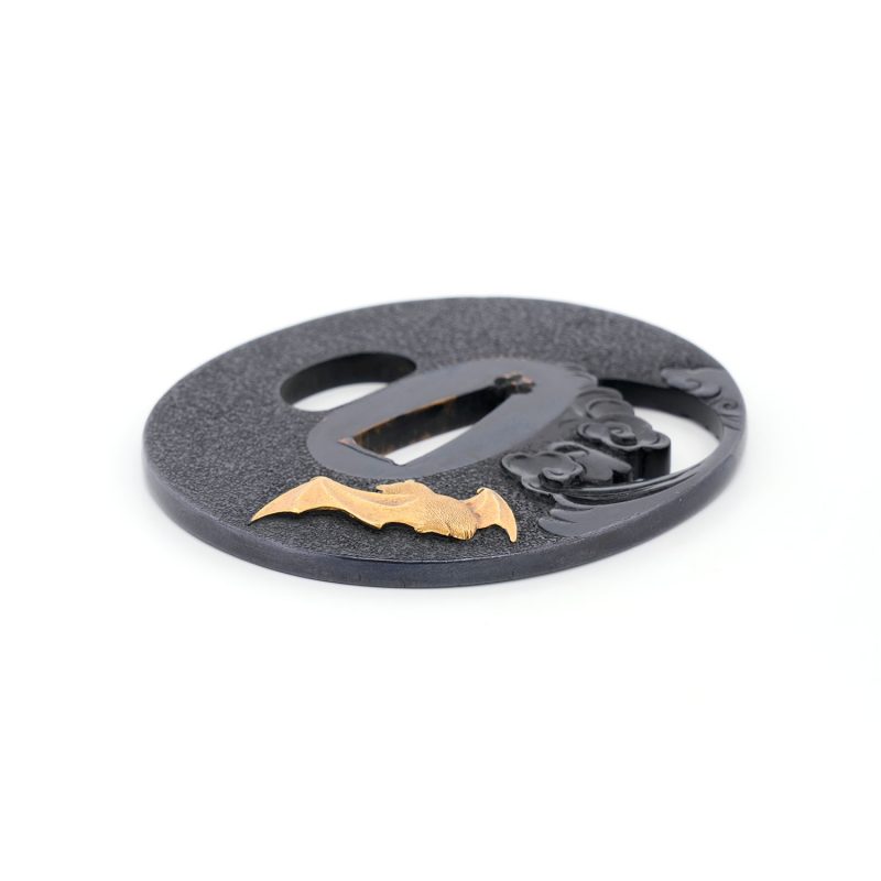 On a richly patinated shakudō ground, hammered with tsuchime to evoke the image of drifting clou ...