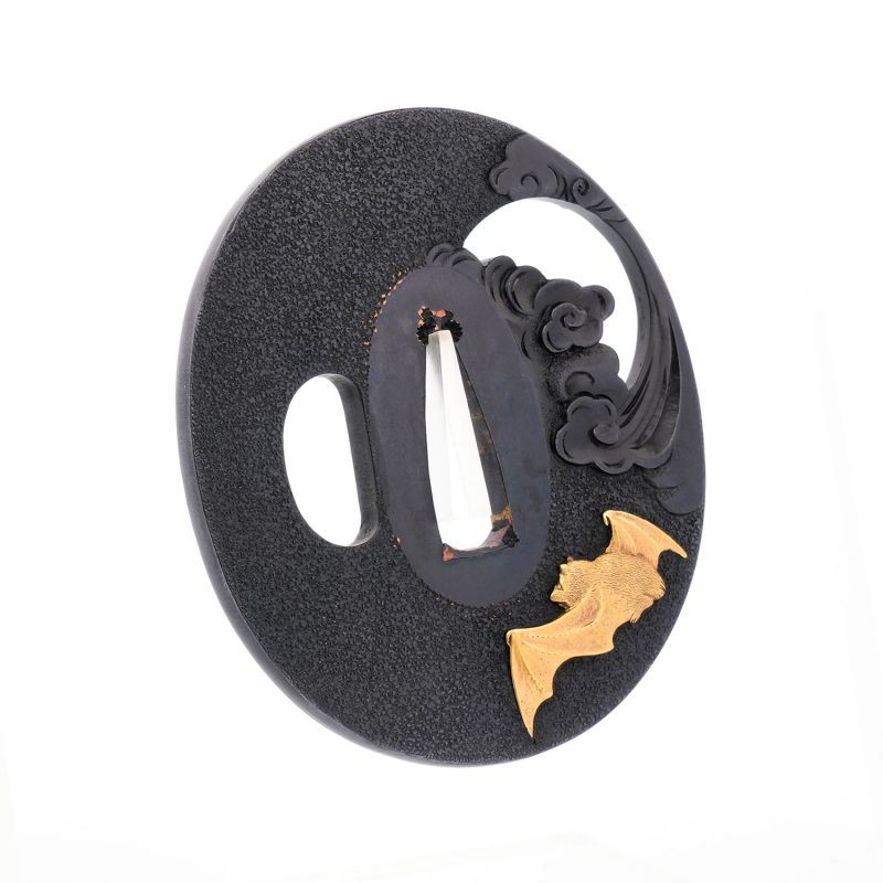 On a richly patinated shakudō ground, hammered with tsuchime to evoke the image of drifting clou ...