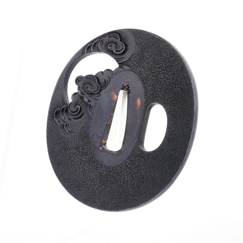On a richly patinated shakudō ground, hammered with tsuchime to evoke the image of drifting clou ...