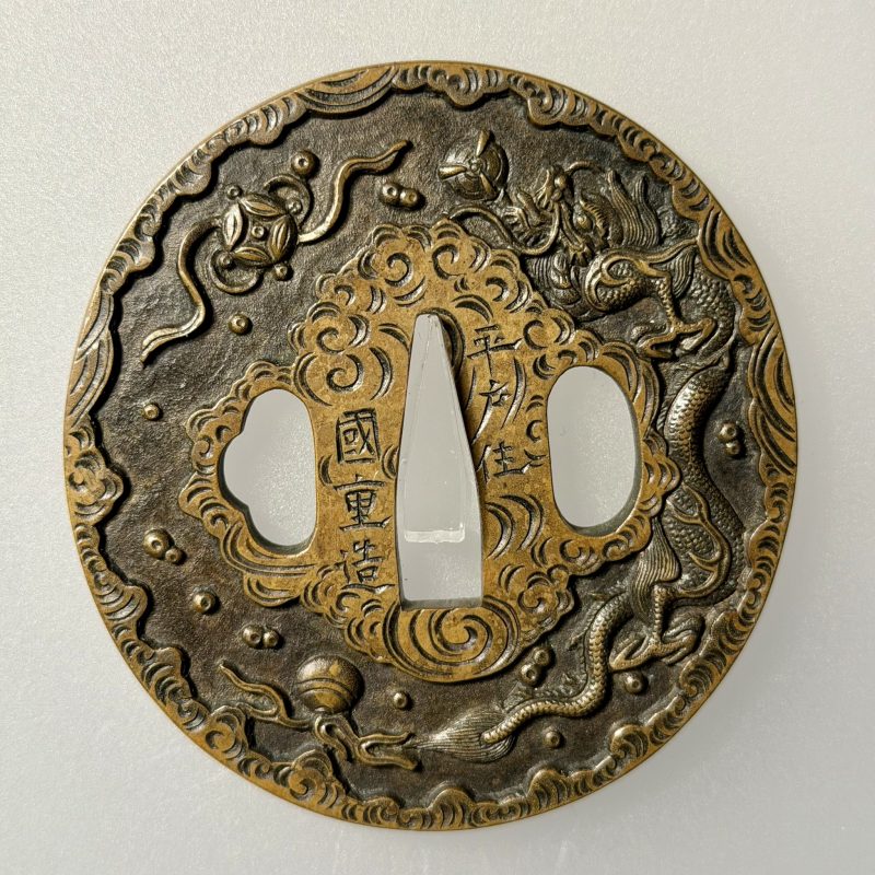 （一）宝珠七宝雲龍図鐔 銘 平戸住 国重造
竪丸形 真鍮石目地 鋤出彫 鋤残耳

→ (1) Tsuba with a desi ...